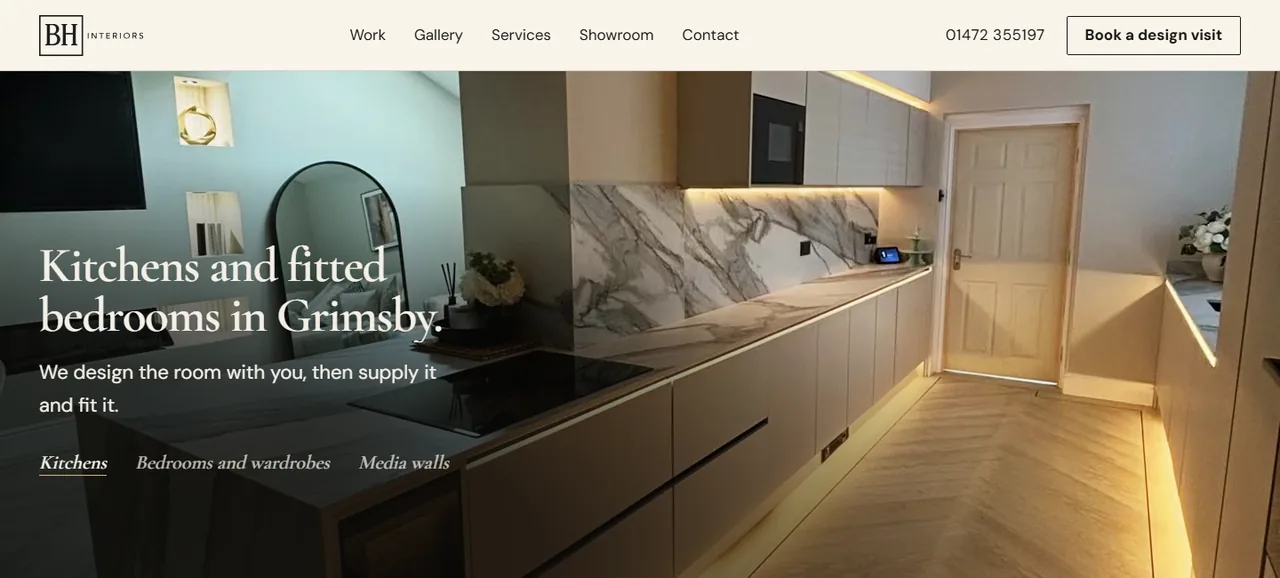 The BH Interiors homepage on a desktop screen, showing a taupe handleless kitchen with a marble splashback and warm lighting under the units